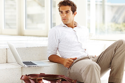Smart young businessman sitting on steps looking away
