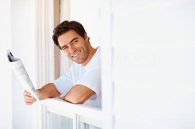Smiling young man with the daily newspaper at the window
