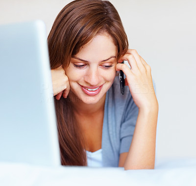 Happy woman in front of laptop on bed and speaking on cellphone