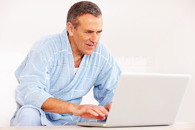 Serious mature man in bathrobe using laptop against white