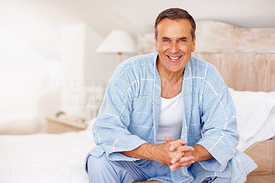 Smiling mature man in bathrobe sitting on bed at home