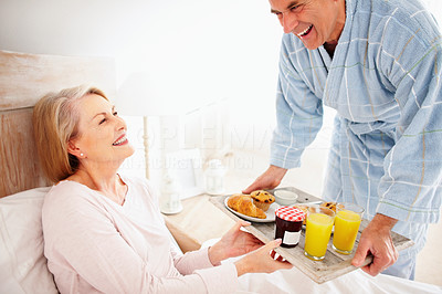 Cheerful mature woman in bed with her husband serving breakfast