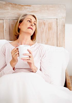 Relaxed mature woman holding coffee mug in bed