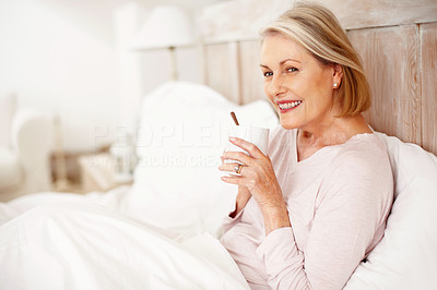 Smiling mature woman having tea or coffee in bed