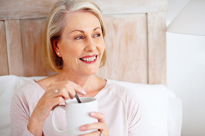 Smiling mature woman stirring tea or coffee while looking away