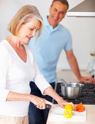 Senior woman preparing food with man in background at kitchen