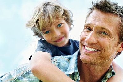 Smiling mature man giving piggyback ride to his son against sky
