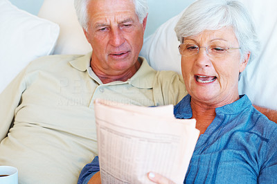 Senior couple relaxing on sofa and reading newspaper