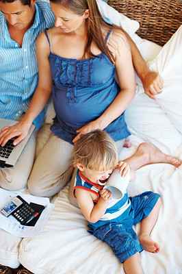 Little boy biting cup handle and parents using laptop
