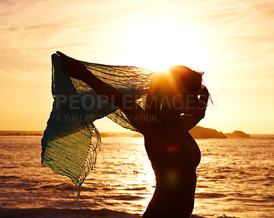 Silhouette image of a fit woman holding up shawl against sunset