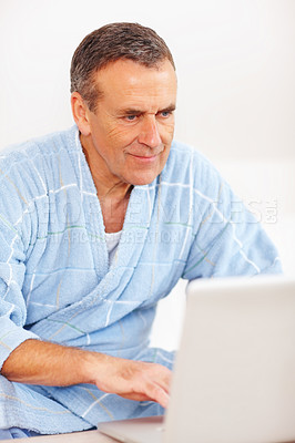 Senior man in bathrobe working on laptop against white