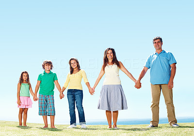 Family holding hands and standing in row against clear blue sky