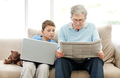 Cute little boy sitting with a laptop while his grandfather reading a newspaper