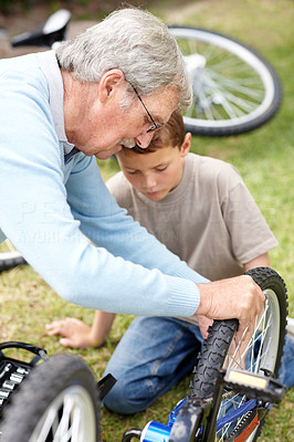 Old man repairing his grandson \'s cycle in a park