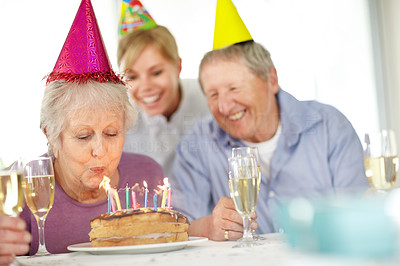 Old woman blowing birthday candles with his family