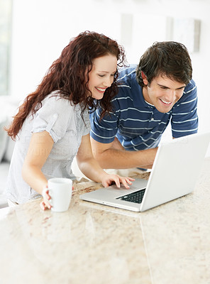 Cute couple drinking coffee and using laptop on kitchen counter