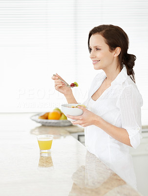 Young woman eating fruit salad at kitchen counter