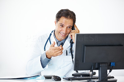 Male physician sitting at desk with computer talking on telephone