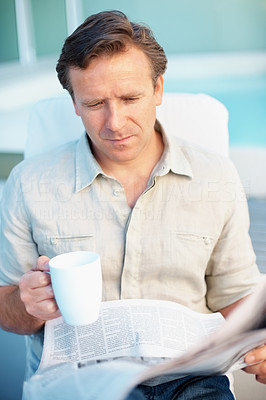 Man drinking coffee while reading a newspaper
