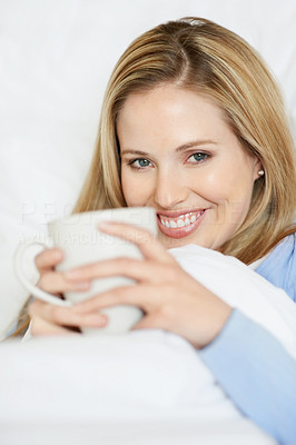 Closeup of a young smiling woman holding a cup of tea in bed