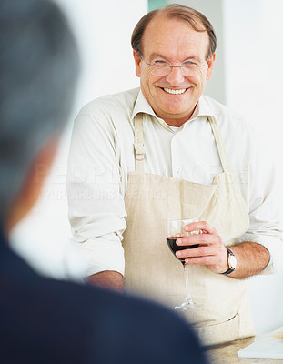Smiling retired man with a wine glass facing wife