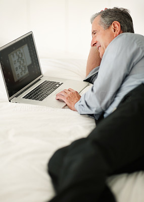 Relaxed mature business man lying in bed while working on laptop