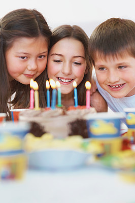 Three friends smiling in front of a lit birthday cake
