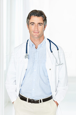 Mature male doctor standing in corridor with hands in pockets