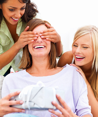 Closeup of young smiling friends covering a happy girl\'s eyes while holding a gift in hands