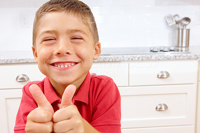 Happy young boy showing thumbs up sign in kitchen