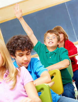 Excited looking boy raised hand in classroom with classmates around