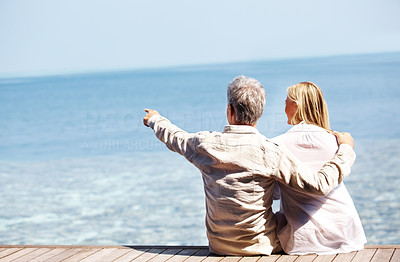 Rear view of mature couple sitting on a boardwalk by the sea
