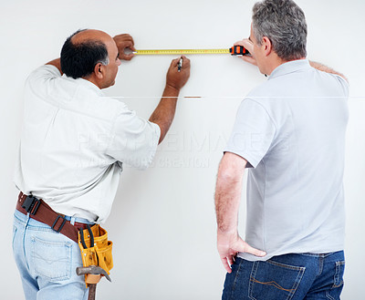 Two contractors using measuring tape to make markings on wall
