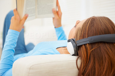 Young female relaxing on the couch reading a book, listening to music