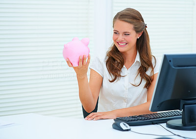 Pretty business woman holding a piggybank while at work