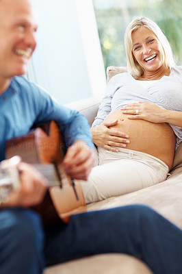 Happy man playing the guitar for his pregnant wife