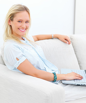 Portrait of a smiling young lady sitting on sofa, using laptop