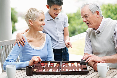 Happy boy watches elderly couple play a game of backgammon