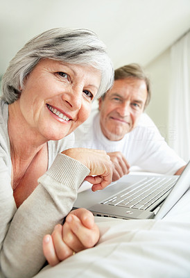 Happy retired woman on bed using a laptop with a man