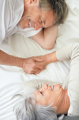 Top view of a smiling elderly couple holding hands in bed