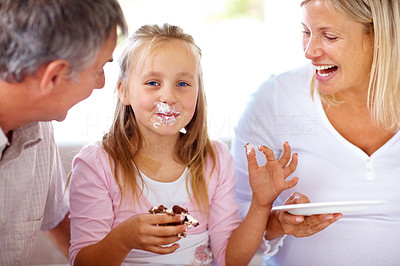 Sweet little girl eating cake with her parents