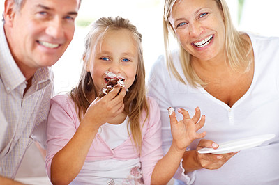Cute little girl eating cake with her parents