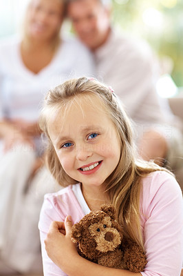 Young girl with teddy bear while her parents sitting at back