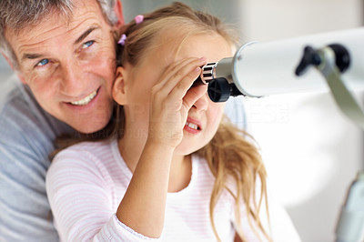 Young girl looking through telescope with father