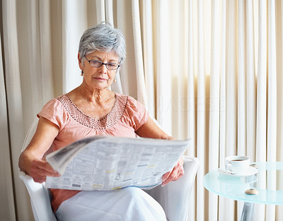 Retired senior woman reading newspaper with a cup of coffee