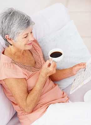 Elderly woman drinking coffee and reading the newspaper