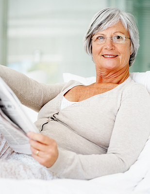 Relaxed senior woman reading newspaper on bed at home