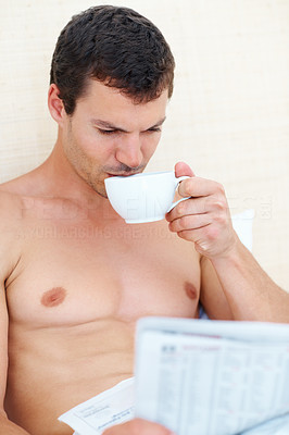 Shirtless man having tea while reading newspaper