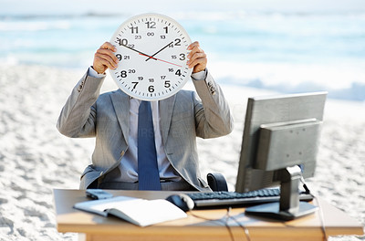 Business man holding wall clock over his face while at his desk