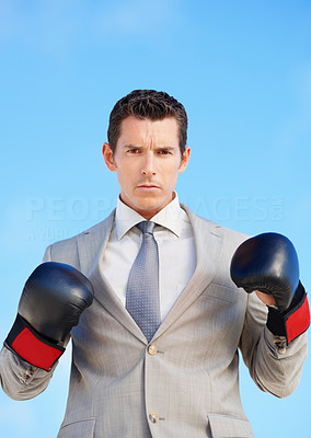 Serious middle aged executive wearing boxing gloves against sky